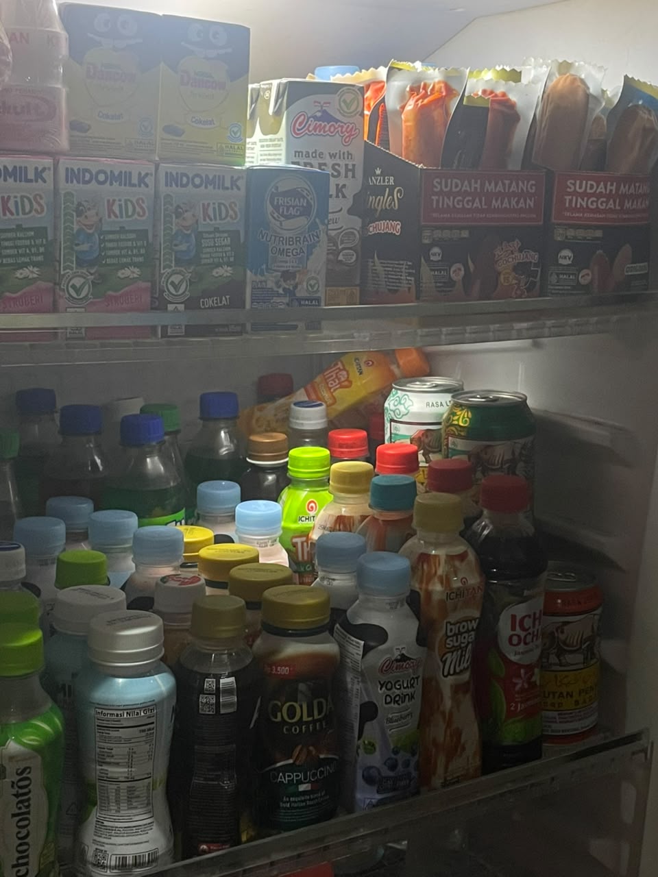 Rak minuman toko berisi minuman botol, kaleng, dan susu kotak